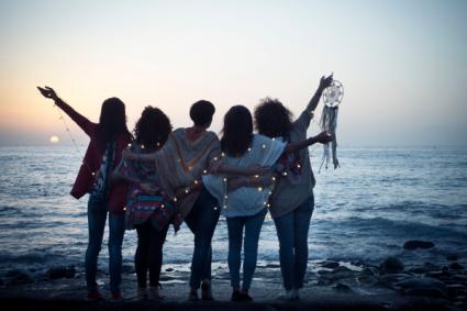 Five friends women hug each other viewed from back looking at the sunset holding light 