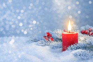 Lighted red candle, pine branches, and holly berries in snow